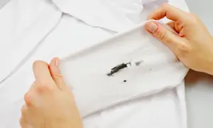 Dłonie pokazują białą koszulkę z plamą po tuszu. Dowiedz się, jak usunąć tusz z ubrania, aby przywrócić mu biel.