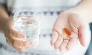 Dłoń trzyma szklankę wody i kapsułkę. Lecytyna na co? Na wsparcie pamięci i koncentracji.