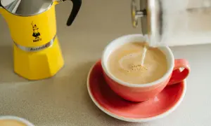 Żółta kawiarka Bialetti obok różowej filiżanki, do której nalewane jest mleko. Idealna kawa z miodem na dobry początek dnia.