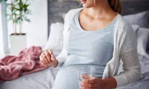 Kobieta w ciąży bierze suplement luteina w ciąży, trzymając w dłoni kapsułkę i szklankę wody.