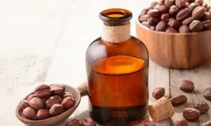 Butelka z bursztynowym płynem, łyżka i miska pełne nasion jojoby. Odkryj niezwykłe olej jojoba właściwości dla Twojej skóry i włosów.
