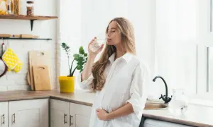 Ciężarna kobieta pije wodę, szukając odpowiedzi, co pić na zgagę w ciąży. Woda to dobry wybór.