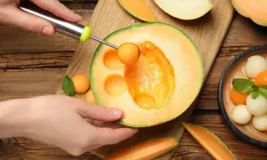 Ręka wydrąża kulki z melona, pokazując, czy melon jest zdrowy. Wokół świeże owoce i listki mięty.