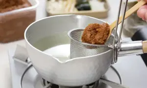 Łyżka z pastą miso jest dodawana do bulionu w garnku. Tak przygotowuje się zupę miso.