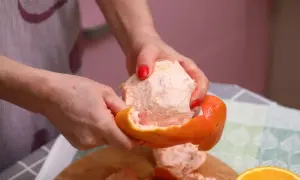 Ręce obierają grejpfruta, pokazując jego soczysty miąższ. Codzienne spożywanie grejpfruta może przynieść wiele korzyści zdrowotnych.