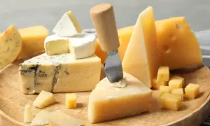 Różne rodzaje serów: pleśniowy, camembert, parmezan i żółty, ułożone na drewnianej desce.
