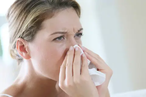 Kobieta z chusteczką przy nosie, szukająca naturalnych sposobów na alergię.