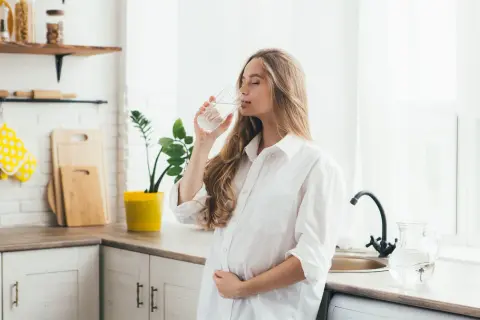 Ciężarna kobieta pije wodę, szukając odpowiedzi, co pić na zgagę w ciąży. Woda to dobry wybór.