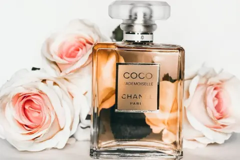 Elegancka butelka Coco Mademoiselle Chanel otoczona różowymi różami. Perfumowana woda toaletowa pachnie dłużej niż woda toaletowa.