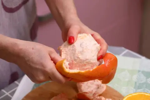 Ręce obierają grejpfruta, pokazując jego soczysty miąższ. Codzienne spożywanie grejpfruta może przynieść wiele korzyści zdrowotnych.