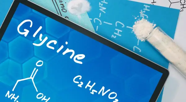 Tablet z napisem "Glycine" i wzorem chemicznym. Obok probówka z białym proszkiem, sugerująca glicyna zastosowanie w chemii.