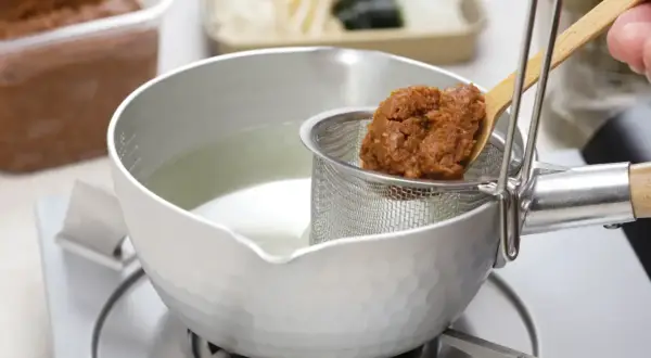 Łyżka z pastą miso jest dodawana do bulionu w garnku. Tak przygotowuje się zupę miso.