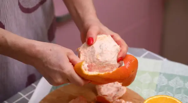 Ręce obierają grejpfruta, pokazując jego soczysty miąższ. Codzienne spożywanie grejpfruta może przynieść wiele korzyści zdrowotnych.