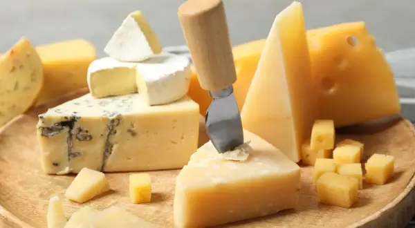 Różne rodzaje serów: pleśniowy, camembert, parmezan i żółty, ułożone na drewnianej desce.