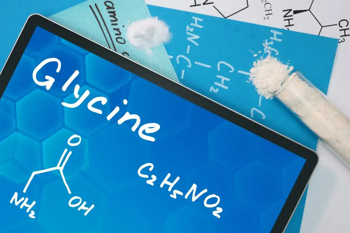Tablet z napisem "Glycine" i wzorem chemicznym. Obok probówka z białym proszkiem, sugerująca glicyna zastosowanie w chemii.