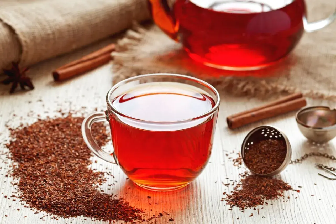 Aromatyczna herbata rooibos, znana ze swoich licznych właściwości, w szklanej filiżance, obok zaparzacza i laski cynamonu.
