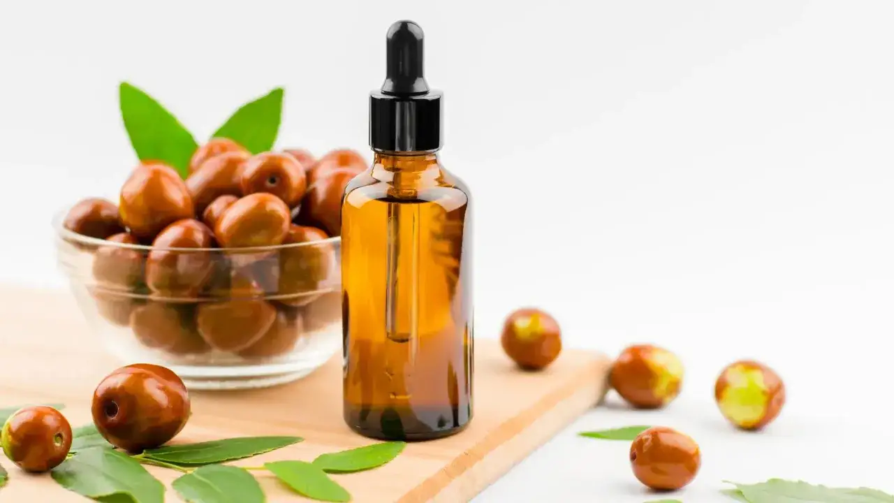 Olej jojoba właściwości: brązowa buteleczka z pipetką i miska pełna owoc&oacute;w jojoby, symbolizujące naturalne piękno i pielęgnację.