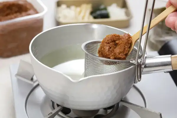 Łyżka z pastą miso jest dodawana do bulionu w garnku. Tak przygotowuje się zupę miso.