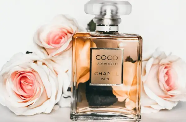 Elegancka butelka Coco Mademoiselle Chanel otoczona różowymi różami. Perfumowana woda toaletowa pachnie dłużej niż woda toaletowa.