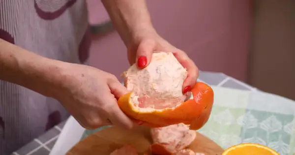 Ręce obierają grejpfruta, pokazując jego soczysty miąższ. Codzienne spożywanie grejpfruta może przynieść wiele korzyści zdrowotnych.