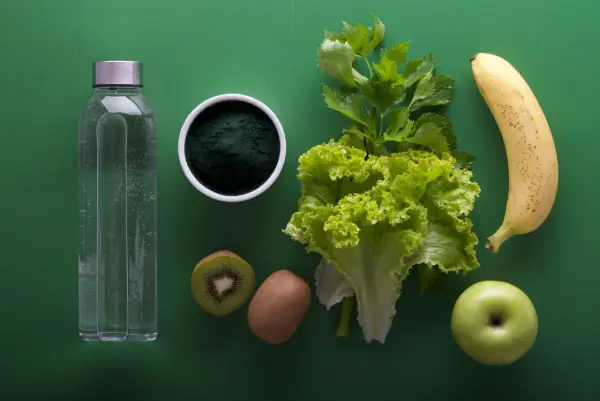 Japońska dieta wodna: butelka wody, spirulina, kiwi, sałata, seler, jabłko i banan na zielonym tle.