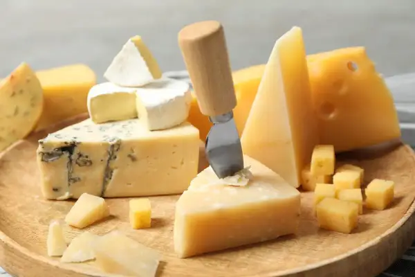 Różne rodzaje serów: pleśniowy, camembert, parmezan i żółty, ułożone na drewnianej desce.